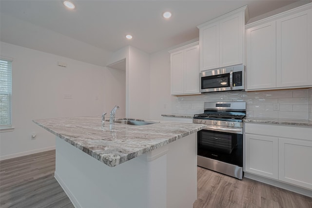 17807 Cappadocia Trl, Tomball, TX 77377 - kitchen with appliances with stainless steel finishes, light wood-style flooring, an island with sink, white cabinetry, and recessed lighting