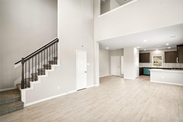 3211 Falling Brook Dr, Baytown, TX 77521 - unfurnished living room featuring light wood-type flooring, stairway, baseboards, a towering ceiling, and recessed lighting