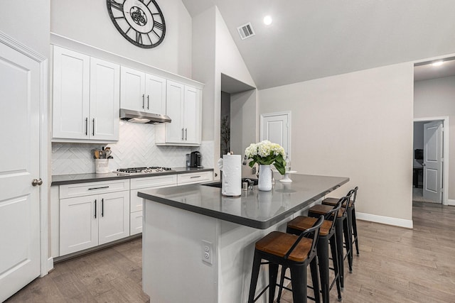3423 Crescent Vista Dr, Fulshear, TX 77441 - kitchen featuring dark countertops, under cabinet range hood, a center island, decorative backsplash, and a breakfast bar area