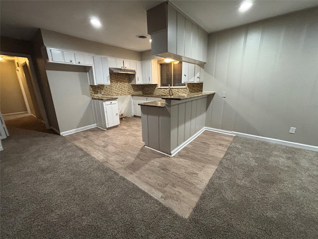1102 Laurentide St, Houston, TX 77029 - kitchen featuring a peninsula, white cabinetry, wood finished floors, decorative backsplash, and under cabinet range hood