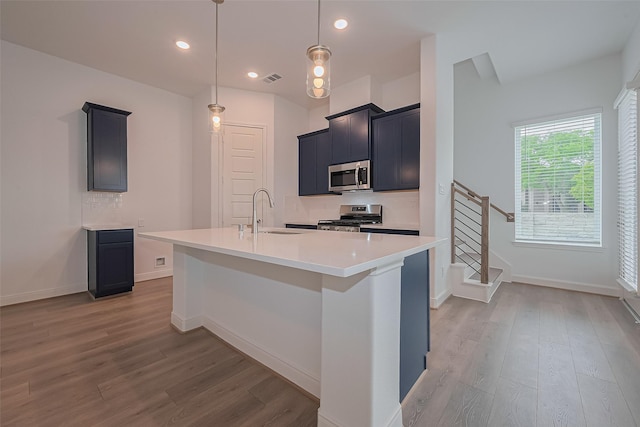 8933 Grovner Pl, Houston, TX 77055 - kitchen featuring appliances with stainless steel finishes, a sink, wood finished floors, light countertops, and a kitchen island with sink