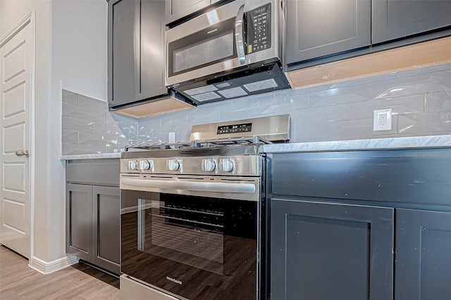 10155 Red Snapper Rd, Magnolia, TX 77354 - kitchen featuring appliances with stainless steel finishes, gray cabinetry, light wood finished floors, decorative backsplash, and light stone counters