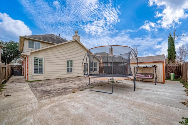 2710 Marigny Dr, Houston, TX 77014 - back of house with a trampoline, a patio area, a fenced backyard, a chimney, and central AC