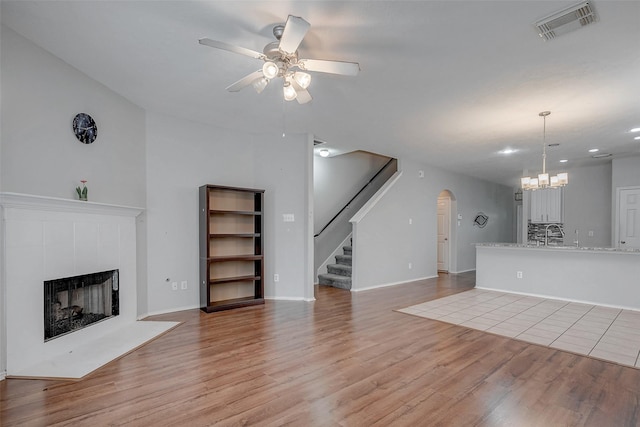 2710 Marigny Dr, Houston, TX 77014 - unfurnished living room with a ceiling fan, stairway, a tiled fireplace, arched walkways, and light wood finished floors