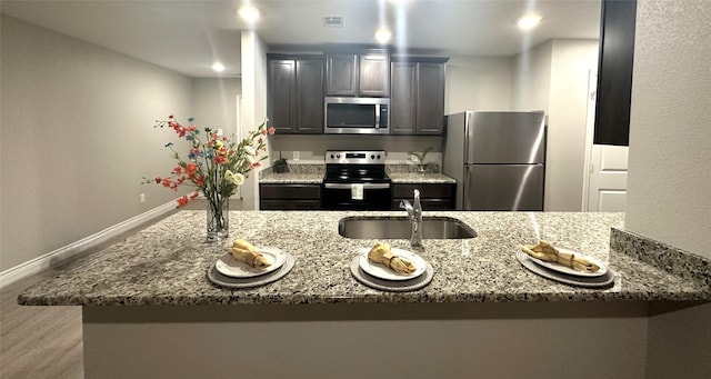 6230 El Cobre Dr, Houston, TX 77048 - kitchen featuring appliances with stainless steel finishes, a sink, light stone counters, wood finished floors, and baseboards