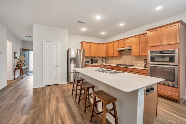 2114 Lost Timbers Dr, Conroe, TX 77304 - kitchen with a sink, appliances with stainless steel finishes, wood finished floors, under cabinet range hood, and tasteful backsplash