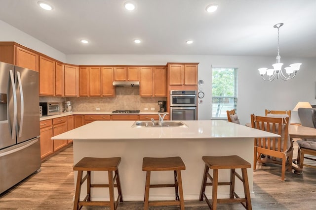 2114 Lost Timbers Dr, Conroe, TX 77304 - kitchen with stainless steel appliances, a sink, light wood-style flooring, a breakfast bar, and backsplash