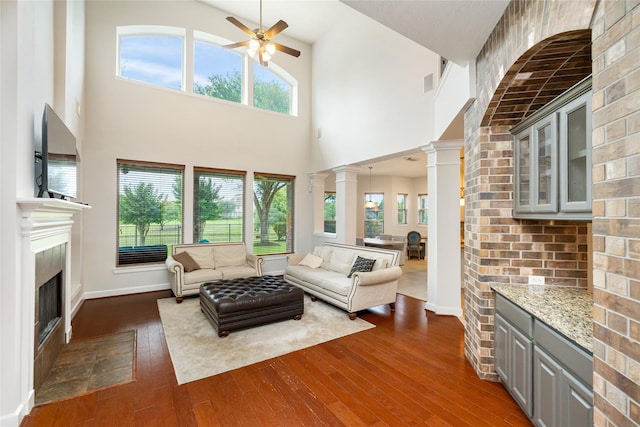 17311 Morgans Lake Dr, Cypress, TX 77433 - living room with dark wood-type flooring, a fireplace with flush hearth, a towering ceiling, ceiling fan, and ornate columns