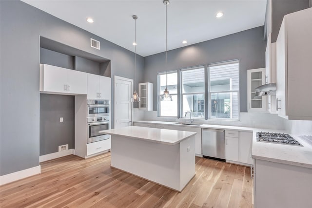 2620 Rusk St, Houston, TX 77003 - kitchen featuring stainless steel appliances, white cabinets, a sink, light wood finished floors, and glass insert cabinets