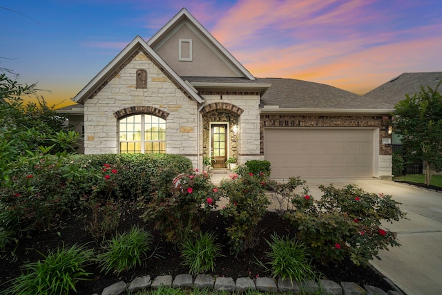 27130 Spanish Wind Ct, Magnolia, TX 77354 - french country style house featuring stone siding, roof with shingles, an attached garage, driveway, and stucco siding