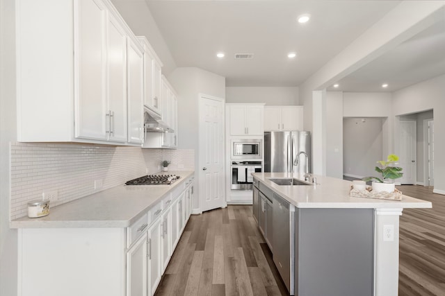 27130 Spanish Wind Ct, Magnolia, TX 77354 - kitchen with stainless steel appliances, a sink, under cabinet range hood, wood finished floors, and recessed lighting