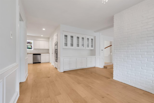13631 Balmore Cir, Houston, TX 77069 - hall featuring light wood finished floors, stairway, brick wall, a wainscoted wall, and a decorative wall