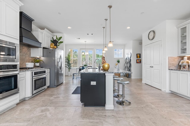 1304 Veranda Mist, League City, TX 77573 - kitchen with stainless steel appliances, light stone counters, decorative backsplash, a kitchen bar, and a center island with sink