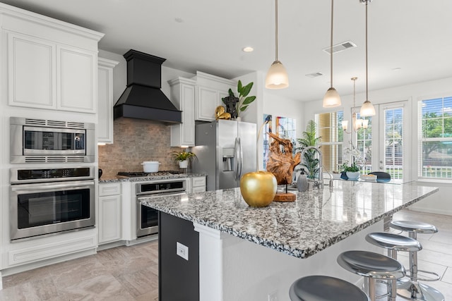 1304 Veranda Mist, League City, TX 77573 - kitchen featuring appliances with stainless steel finishes, custom range hood, backsplash, light stone counters, and a kitchen bar