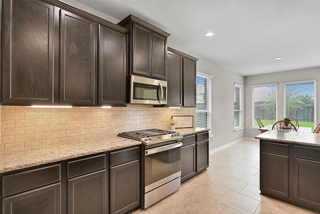 2708 Merlin Ln, Pearland, TX 77581 - kitchen featuring stainless steel appliances, tasteful backsplash, light tile patterned floors, dark brown cabinetry, and light stone countertops