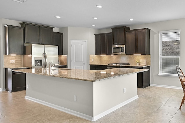 2708 Merlin Ln, Pearland, TX 77581 - kitchen featuring stainless steel appliances, an island with sink, decorative backsplash, light tile patterned flooring, and light stone countertops