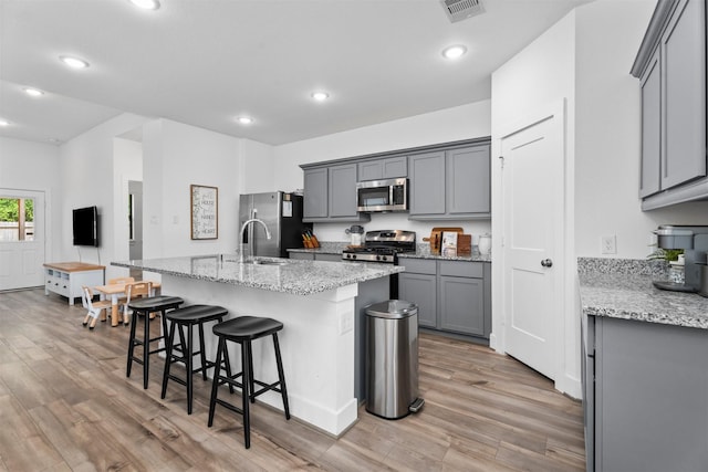 19180 Cedar Lennox Cir, Magnolia, TX 77355 - kitchen with appliances with stainless steel finishes, gray cabinets, light wood-style flooring, a kitchen breakfast bar, and a center island with sink