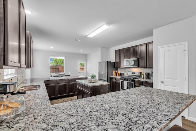 25424 Grotto Falls Ln, Porter, TX 77365 - kitchen featuring appliances with stainless steel finishes, dark brown cabinetry, a sink, a peninsula, and light wood-style flooring