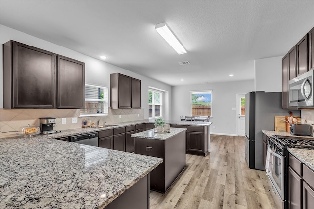 25424 Grotto Falls Ln, Porter, TX 77365 - kitchen with appliances with stainless steel finishes, a peninsula, a kitchen island, dark brown cabinetry, and decorative backsplash
