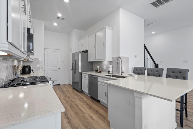 4050 Champlain Way, Rosharon, TX 77583 - kitchen with appliances with stainless steel finishes, a sink, a peninsula, a breakfast bar, and light wood-style flooring