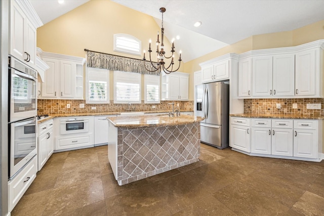 2215 Timbershade Ct, Magnolia, TX 77355 - kitchen featuring appliances with stainless steel finishes, a chandelier, tasteful backsplash, white cabinetry, and high vaulted ceiling