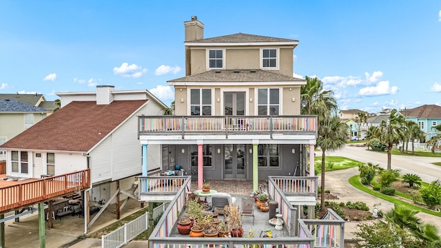 1854 Tiki Dr, Tiki Island, TX 77554 - rear view of house with stucco siding, french doors, a chimney, a balcony, and a wooden deck