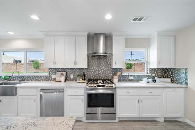 4003 Mischire Dr, Houston, TX 77025 - kitchen featuring appliances with stainless steel finishes, wall chimney exhaust hood, a sink, light countertops, and white cabinetry