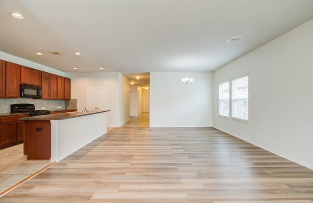 3102 Gianna Springs Ct, Humble, TX 77396 - kitchen with black microwave, gas range, a chandelier, backsplash, and an island with sink