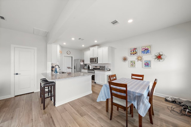 14122 Freeboard Dr, Santa Fe, TX 77510 - kitchen with appliances with stainless steel finishes, a kitchen bar, a peninsula, light wood-style flooring, and white cabinets