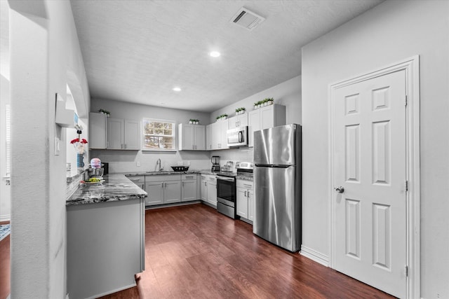 9307 Seeker St, Houston, TX 77028 - kitchen featuring appliances with stainless steel finishes, dark wood-style floors, a sink, recessed lighting, and stone counters