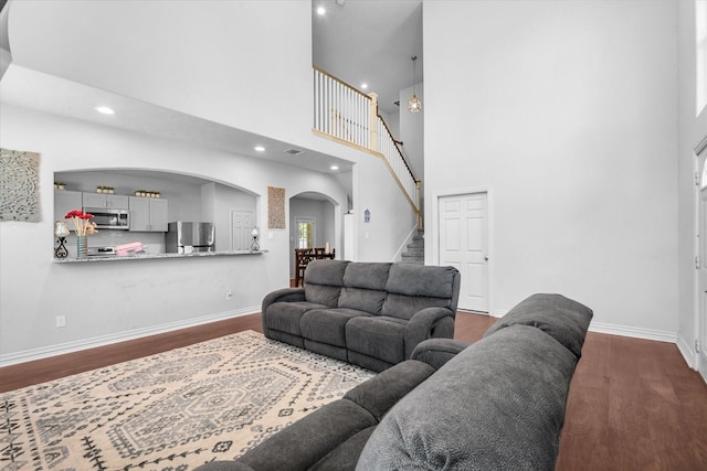 9307 Seeker St, Houston, TX 77028 - living room featuring arched walkways, dark wood-style floors, stairway, baseboards, and a high ceiling