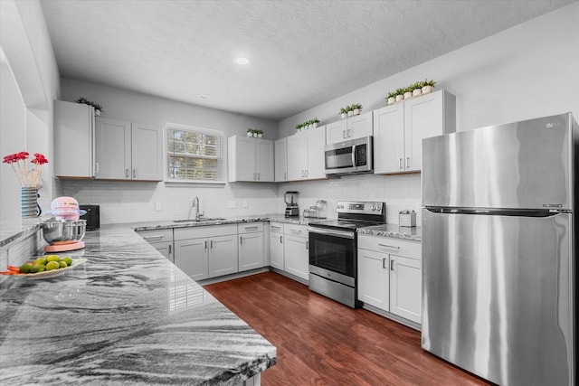 9307 Seeker St, Houston, TX 77028 - kitchen featuring appliances with stainless steel finishes, a sink, light stone countertops, dark wood-style flooring, and backsplash