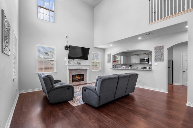 9307 Seeker St, Houston, TX 77028 - living room featuring a towering ceiling, dark wood-type flooring, a tile fireplace, arched walkways, and baseboards