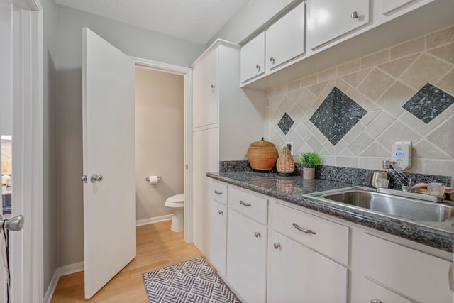 2828 S Logrun Cir, The Woodlands, TX 77380 - kitchen featuring a sink, backsplash, light wood-type flooring, white cabinets, and baseboards