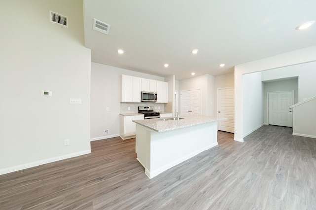 13228 Musky Dr, Conroe, TX 77384 - kitchen with stainless steel appliances, white cabinetry, light wood-type flooring, an island with sink, and recessed lighting