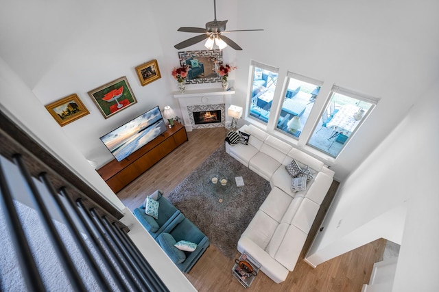 4818 Nodding Thistle Trl, Fulshear, TX 77441 - living room featuring a high ceiling, a warm lit fireplace, wood finished floors, and ceiling fan