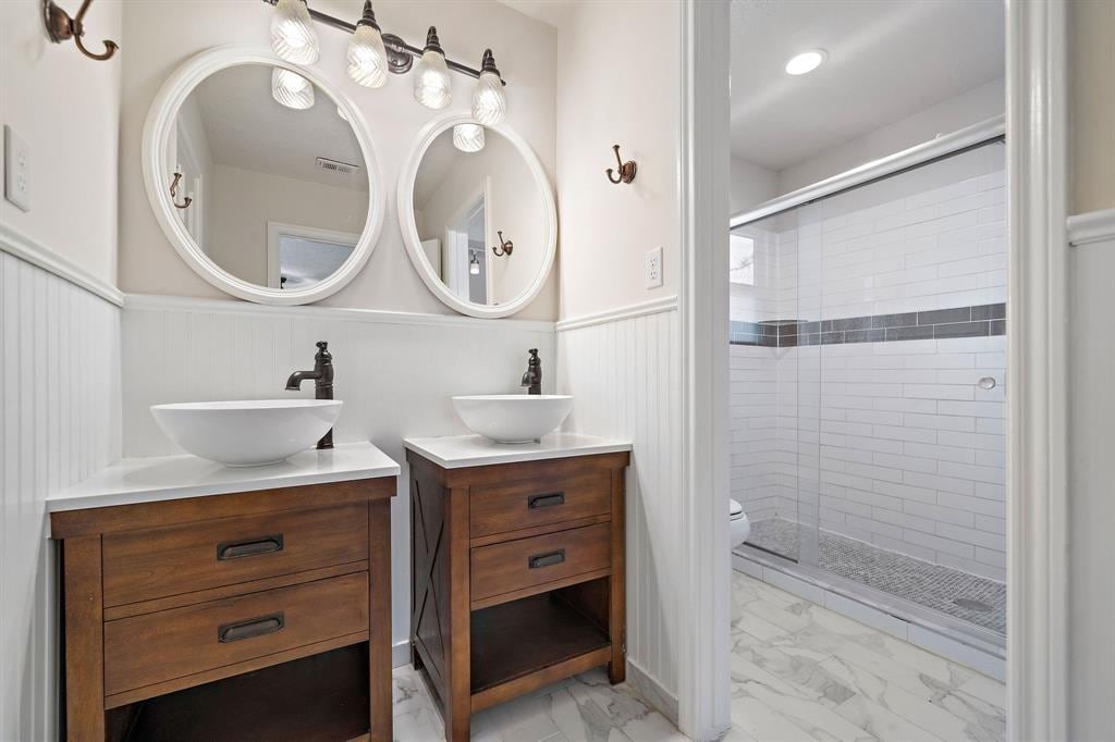 6302 Hickorycrest Dr, Spring, TX 77389 - bathroom featuring marble look tile flooring, a wainscoted wall, a shower stall, two vanities, and toilet