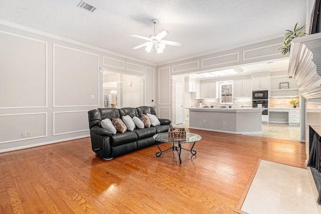 3506 Park Springs Ln, Houston, TX 77345 - living room with a decorative wall, ceiling fan, a fireplace with flush hearth, light wood-type flooring, and crown molding