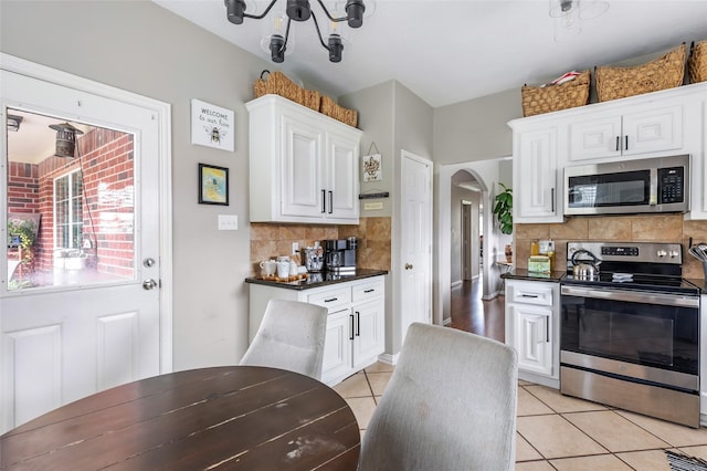 19715 Desna Dr, Porter, TX 77365 - kitchen featuring appliances with stainless steel finishes, dark countertops, light tile patterned floors, tasteful backsplash, and arched walkways