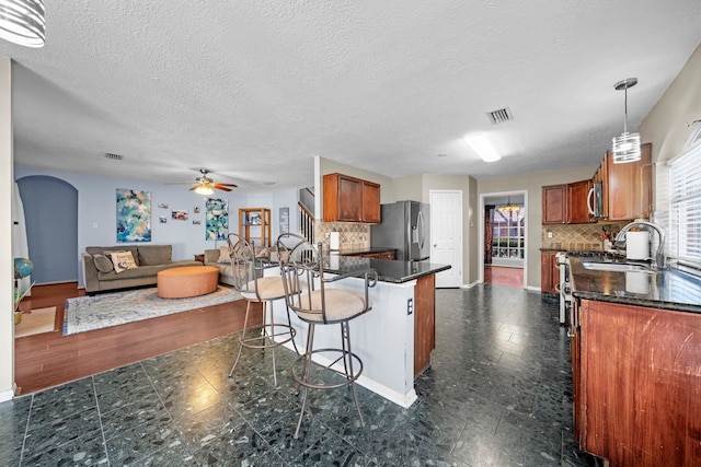 1802 Moston Dr, Spring, TX 77386 - kitchen with stainless steel appliances, brown cabinets, tasteful backsplash, arched walkways, and a textured ceiling