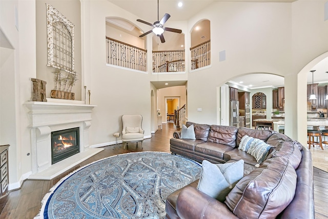 1013 Bolivar Point Ln, Friendswood, TX 77546 - living area with arched walkways, ceiling fan, a glass covered fireplace, wood finished floors, and a high ceiling