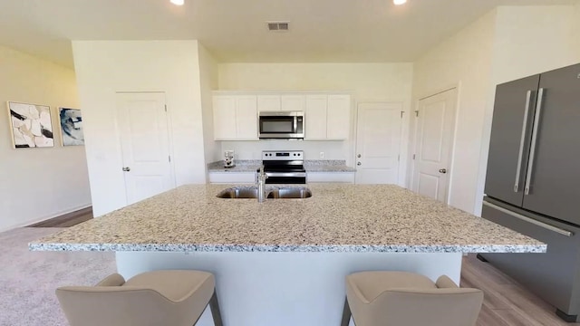 18749 Lucas Michael Way, New Caney, TX 77357 - kitchen featuring stainless steel appliances, a sink, light stone counters, a center island with sink, and white cabinetry