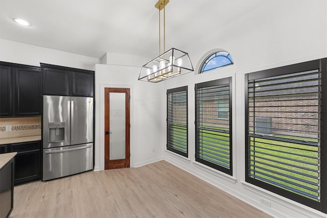 28411 Calaveras Creek Ct, Houston, TX 77336 - kitchen with stainless steel fridge, dark cabinetry, light countertops, light wood-style floors, and decorative light fixtures