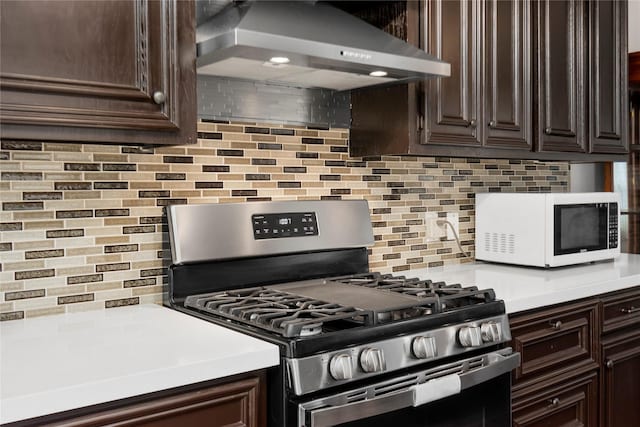 2639 Cypress Island Dr, Houston, TX 77073 - kitchen featuring stainless steel gas range oven, white microwave, ventilation hood, dark brown cabinetry, and backsplash