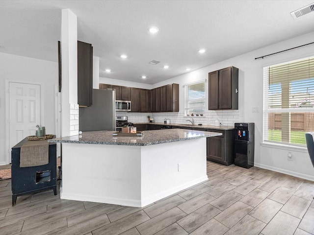 15618 Cliffside Arbor Ln, Houston, TX 77044 - kitchen featuring stainless steel appliances, wood tiled floors, dark stone counters, dark brown cabinets, and backsplash