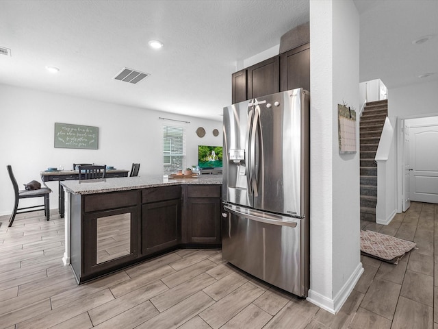 15618 Cliffside Arbor Ln, Houston, TX 77044 - kitchen with stainless steel fridge with ice dispenser, wood tiled floors, dark brown cabinetry, light stone countertops, and recessed lighting
