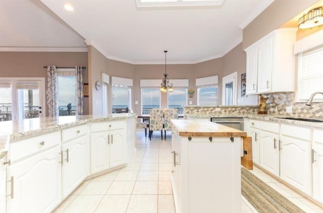 423 Hana Dr, Tiki Island, TX 77554 - kitchen featuring a sink, butcher block counters, a kitchen island, light tile patterned flooring, and crown molding