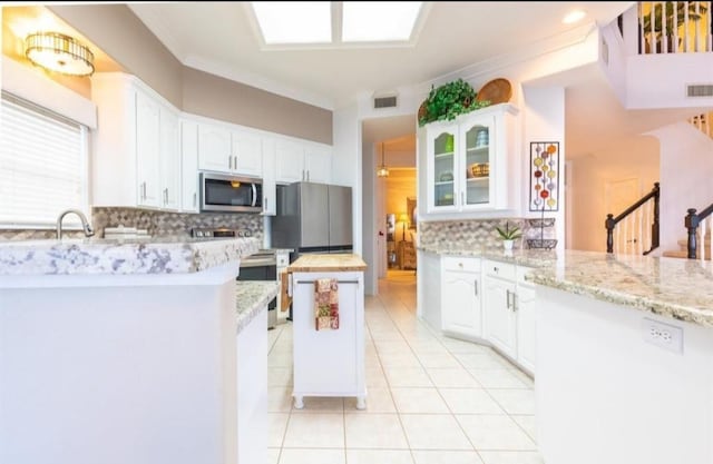 423 Hana Dr, Tiki Island, TX 77554 - kitchen with appliances with stainless steel finishes, decorative backsplash, ornamental molding, light tile patterned floors, and white cabinetry