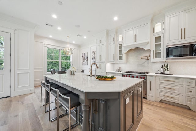 432 Marshall St, Houston, TX 77006 - kitchen featuring built in microwave, high end stainless steel range oven, a large island with sink, light wood-style flooring, and a sink