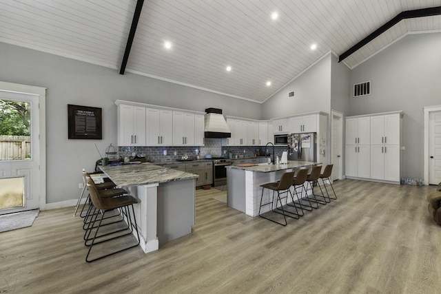 19885 Keenan Cut Off Rd, Montgomery, TX 77316 - kitchen with a kitchen bar, appliances with stainless steel finishes, custom range hood, high vaulted ceiling, and white cabinetry